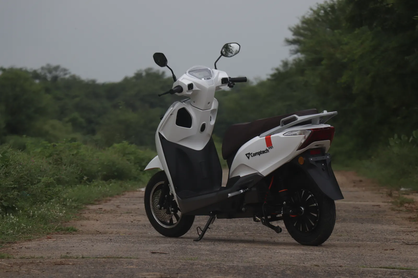 A Comptech electric scooter on an open tree-lined road